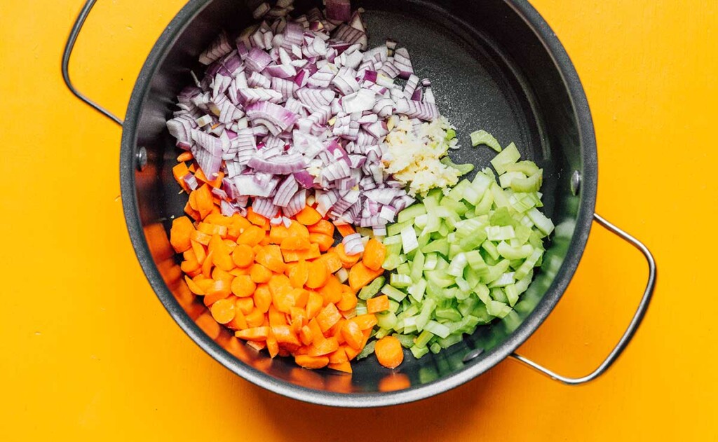 A large pot filled with olive oil and diced red onion, celery, and carrots