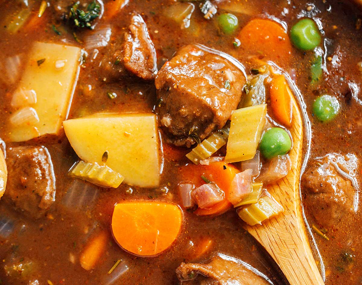 A close-up view of a wooden spoon in a bowl of vegan beef stew