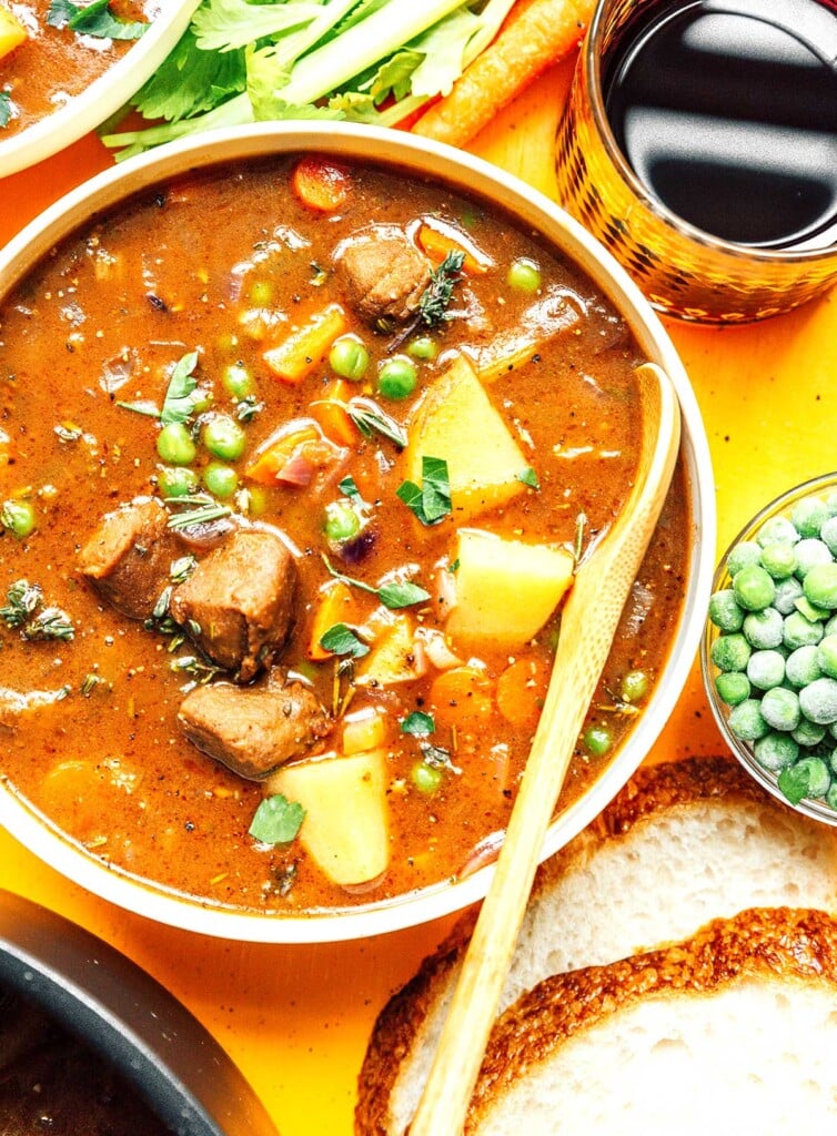 A bowl of vegan beef stew surrounded by various stew ingredients 