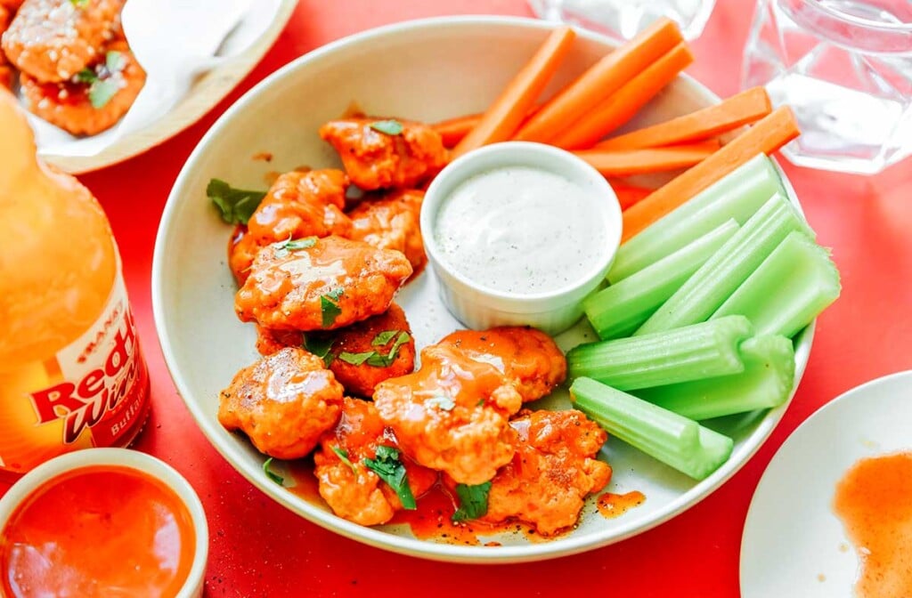 A plate filled with seitan wings, celery, and dipping sauce surrounded by various ingredients 