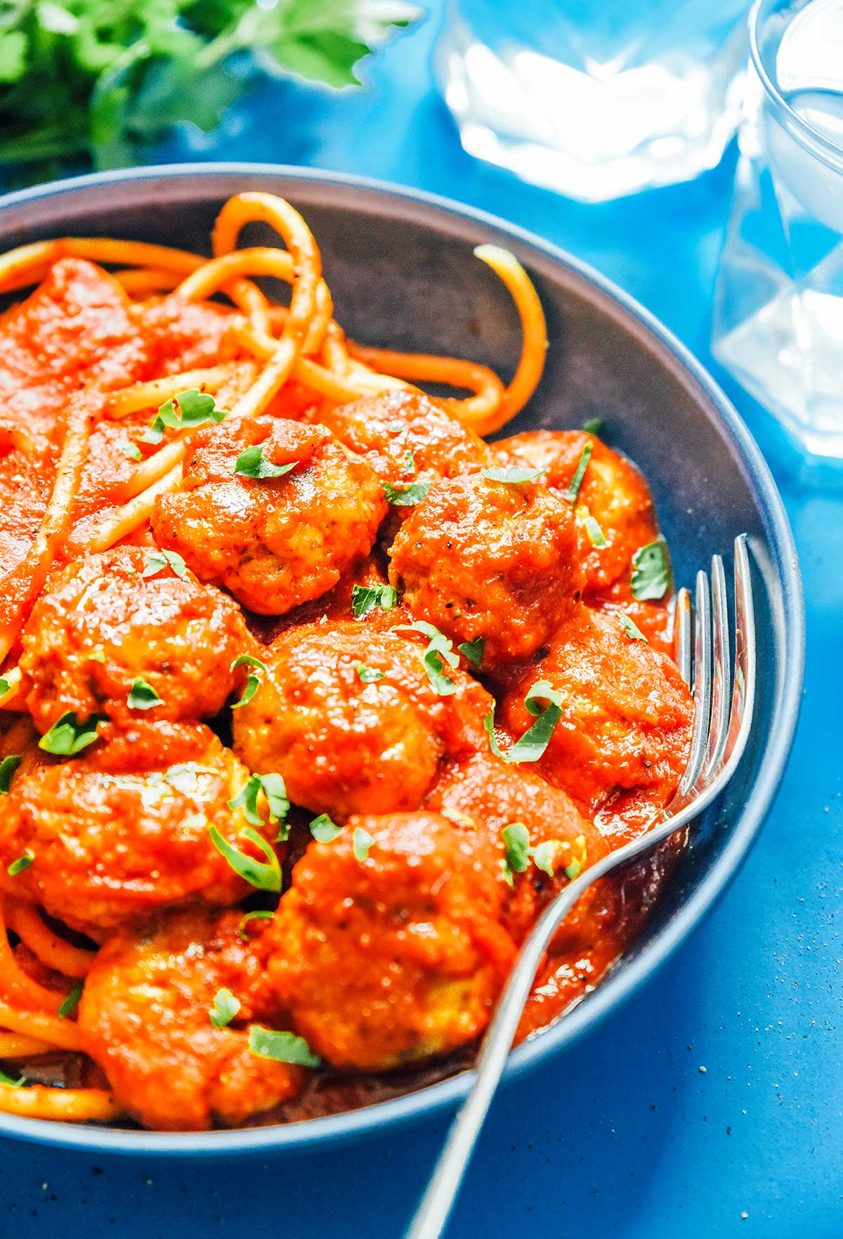 A blue ceramic bowl filled with pasta, marinara sauce, and seitan plant-based meatballs
