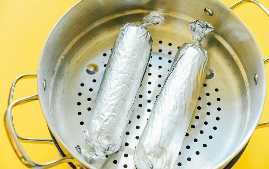 Two vegan pepperoni logs wrapped in tin foil and placed in a simmer basket