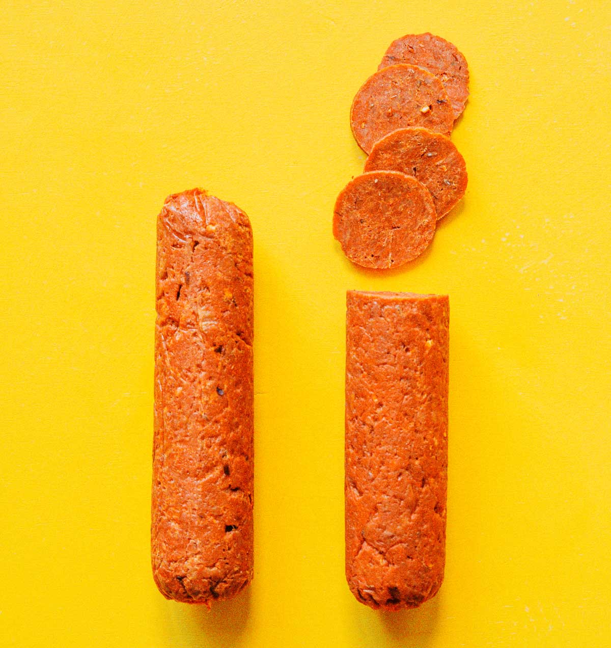 Two logs of vegan pepperoni side by side on a yellow background