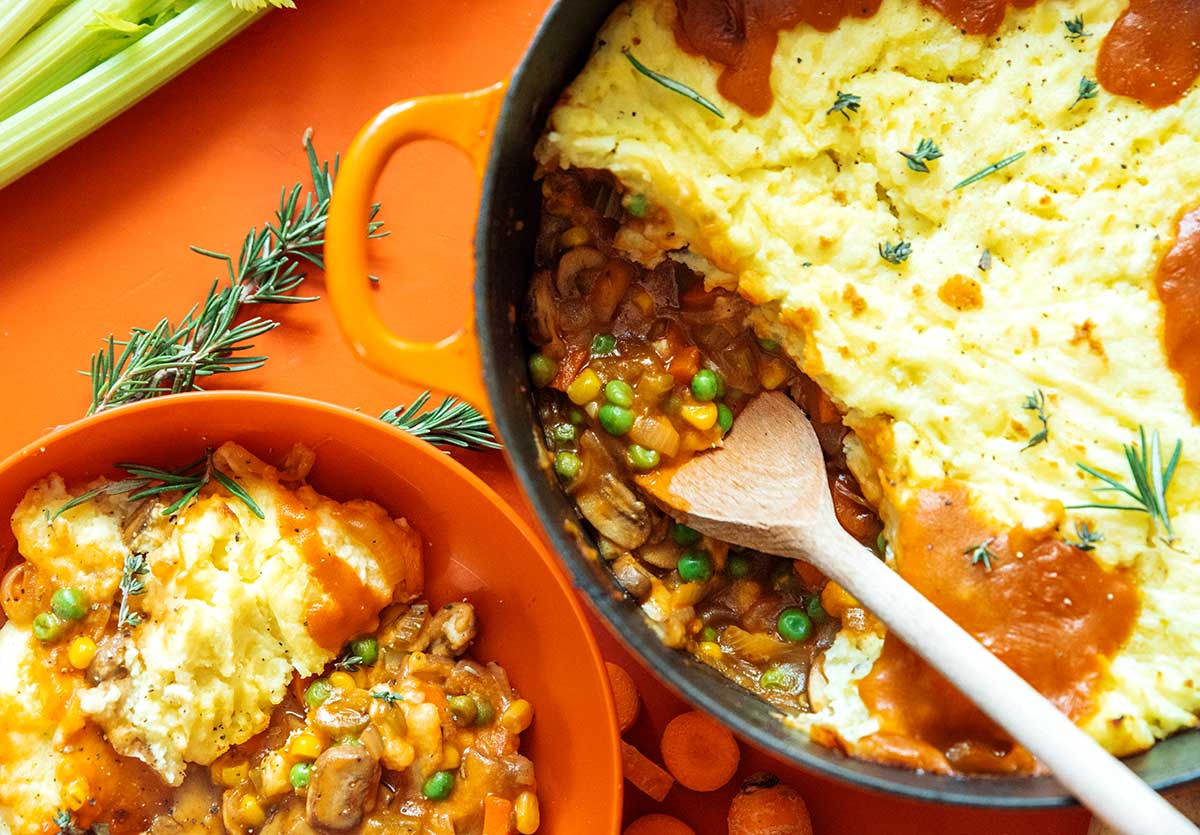 A pot filled with freshly cooked vegetarian shepard's pie next to an orange bowl filled with a serving