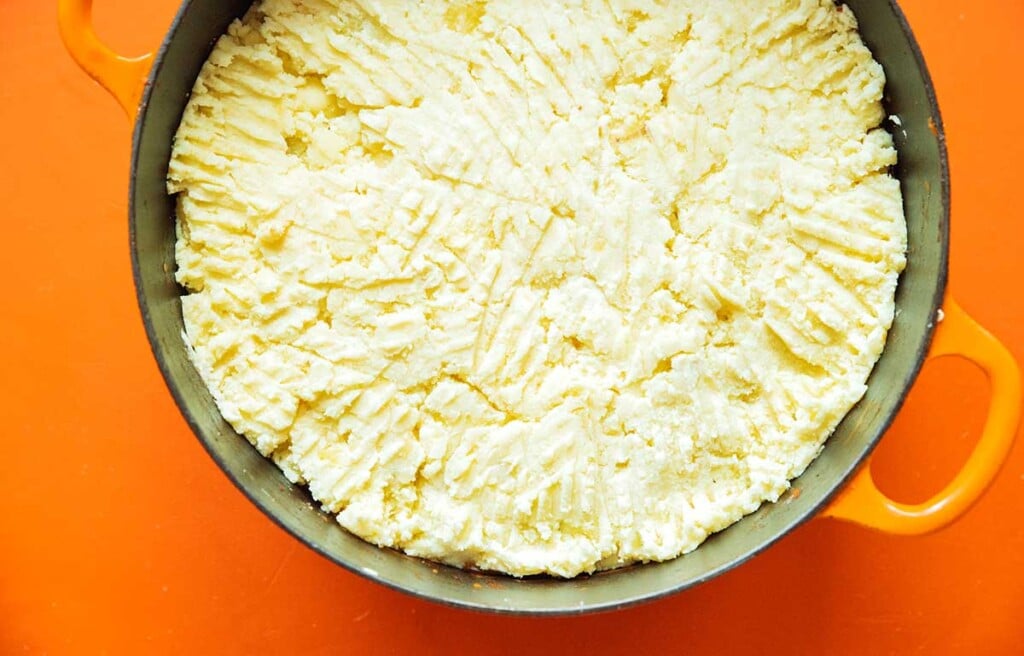 A large pot filled with veggie shepard's pie ingredients with mashed potatoes spread out on top