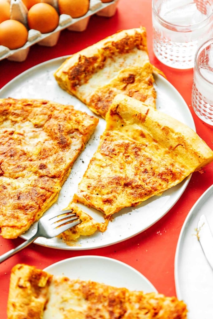 Three slices of French toast pizza on a white plate with a fork grabbing a piece from one of the slices