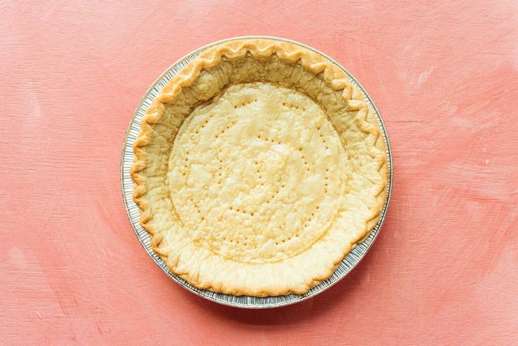 A fresh out of the oven, golden brown empty pie crust in a tin cooking tray on a light pink background