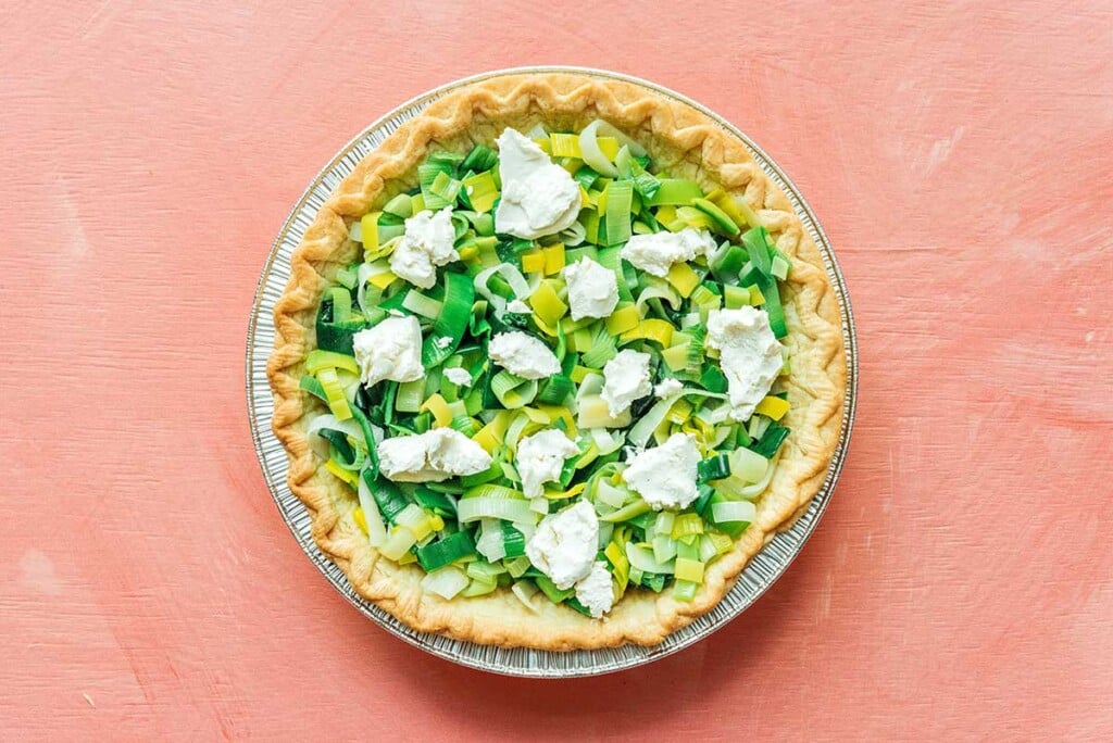 A cooked pie crust filled with sliced leeks with goat cheese pieces on top