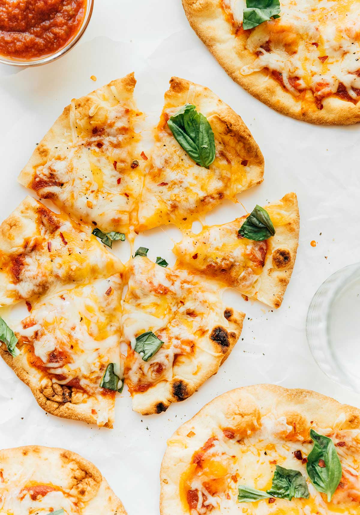 A naan pizza topped with sauce, mozzarella cheese, and fresh basil and sliced into 6 pieces