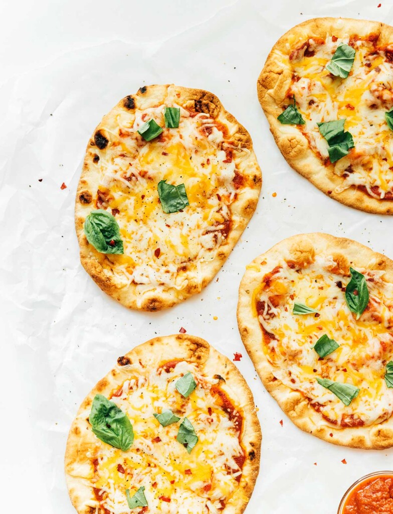 Four naan pizzas topped with sauce, mozzarella cheese, and fresh basil