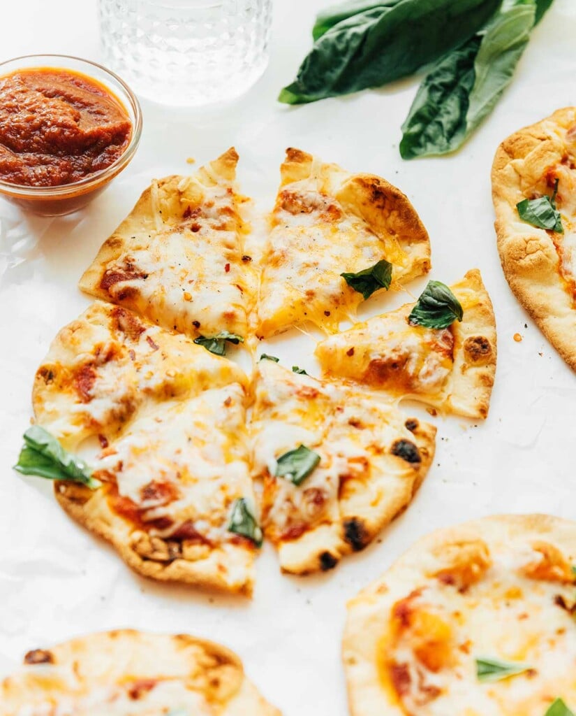 A naan pizza topped with sauce, mozzarella cheese, and fresh basil and sliced into 6 pieces