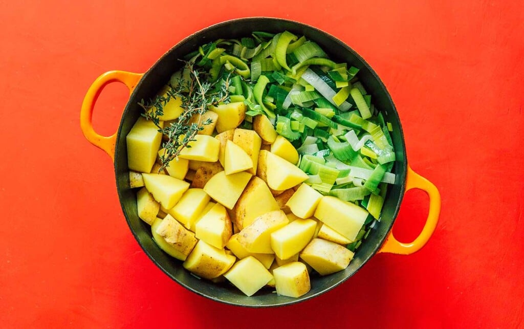 A large pot filled with leek slices, chopped potatoes, and thyme