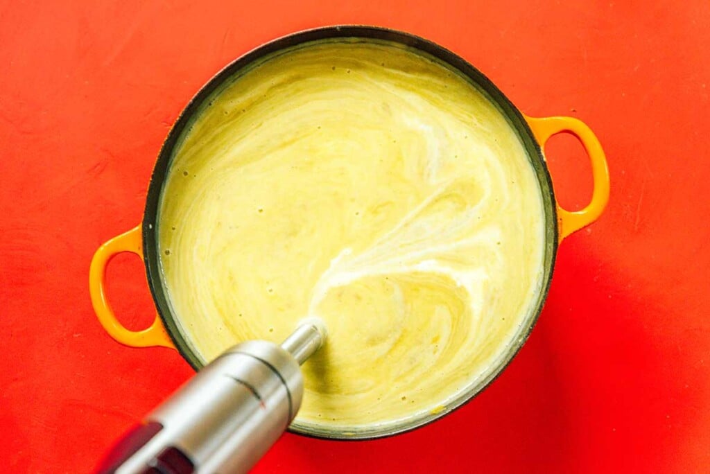 Using an immersion blender to blend a large pot filled with potato leek soup ingredients