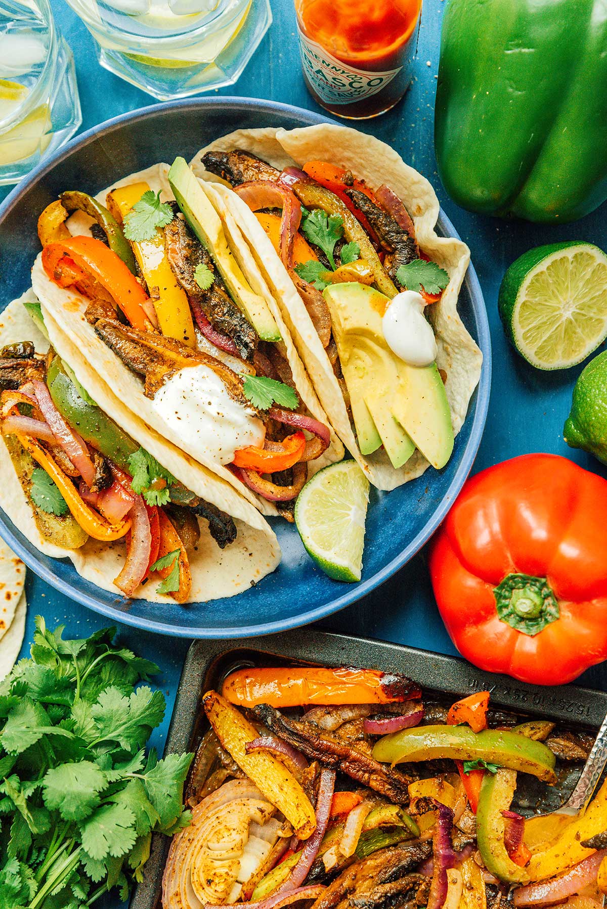 A blue plate filled with 3 vegetable fajitas and surrounded by various fajita ingredients