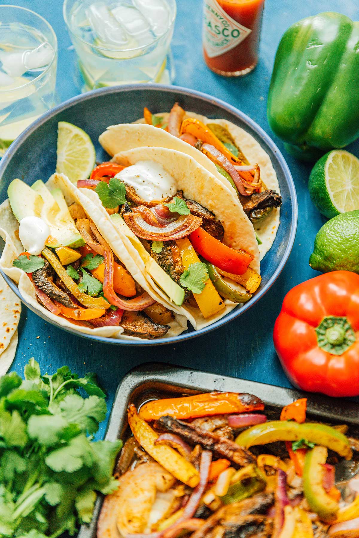 A blue plate filled with 3 veggie fajitas and surrounded by various fajita ingredients