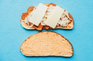 Open sandwich with rye bread; top half piled high with corned beef, sauerkraut, and Swiss cheese; bottom half spread generously with dressing. Perfect twist on a classic Reuben, even tempting for those eyeing a vegetarian version; served on a light blue surface.