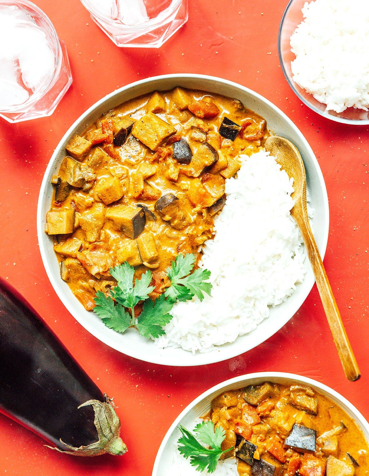 A white bowl filled with eggplant curry, white rice, and cilantro