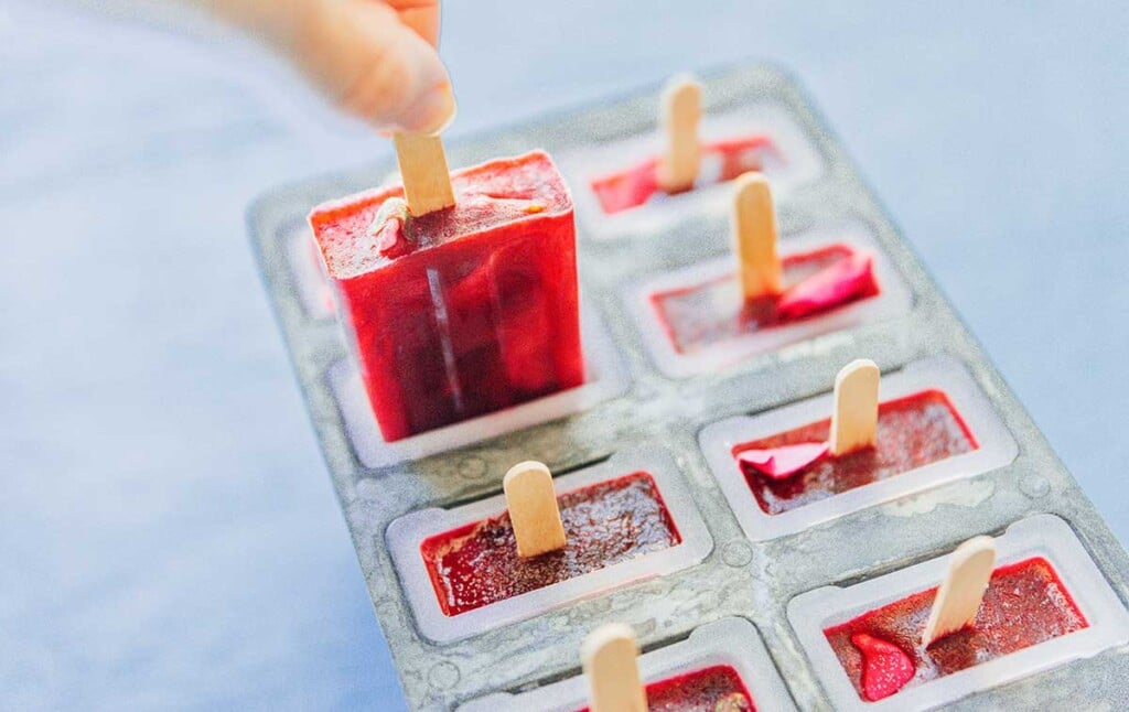 A hand removing a hibiscus popsicle from a popsicle mold