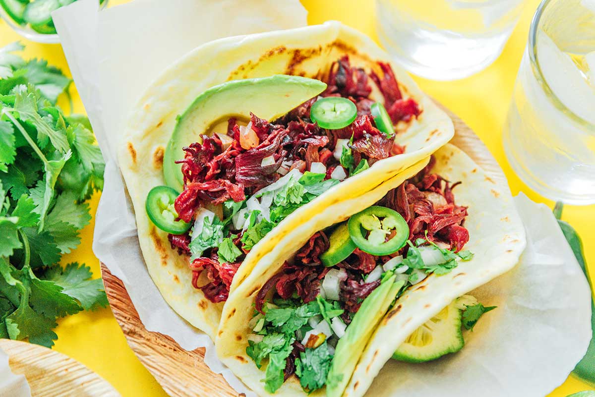 Two hibiscus tacos assembled on a wooden plate
