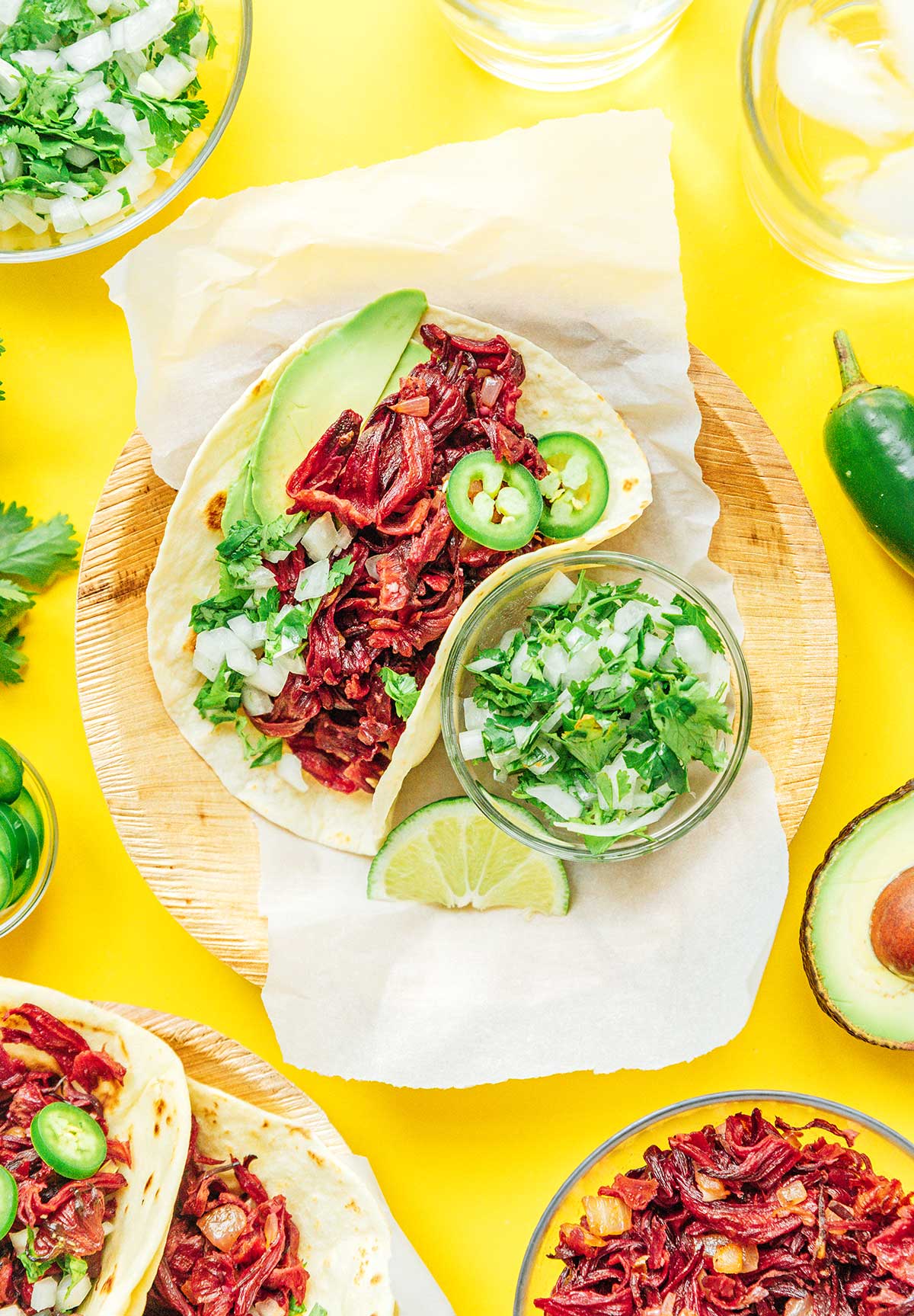 A hibiscus taco on a wooden plate alongside a bowl of onion and cilantro relish and one lime slice