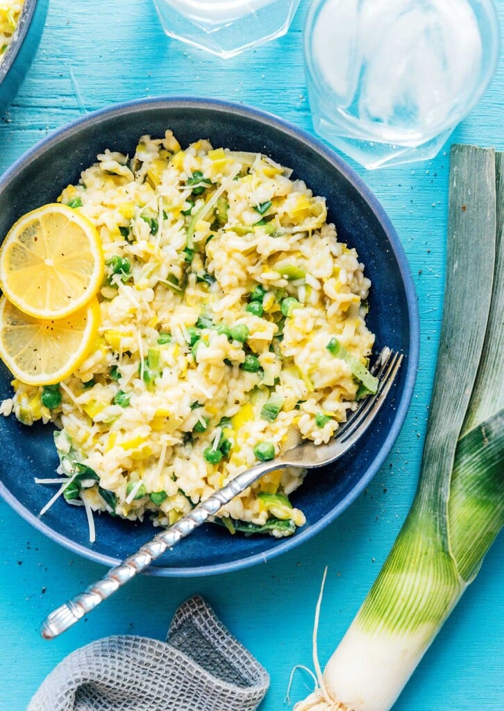 A blue bowl filled with leek risotto and topped with lemon slices