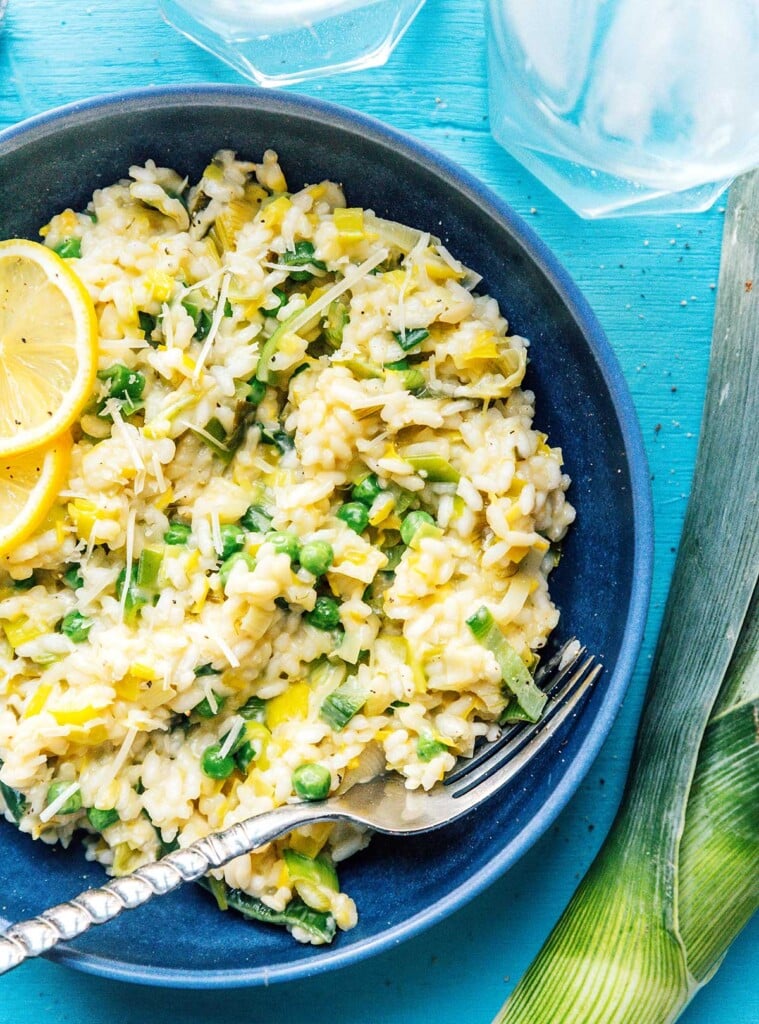 A close up view of a blue bowl filled with leek risotto and topped with lemon slices