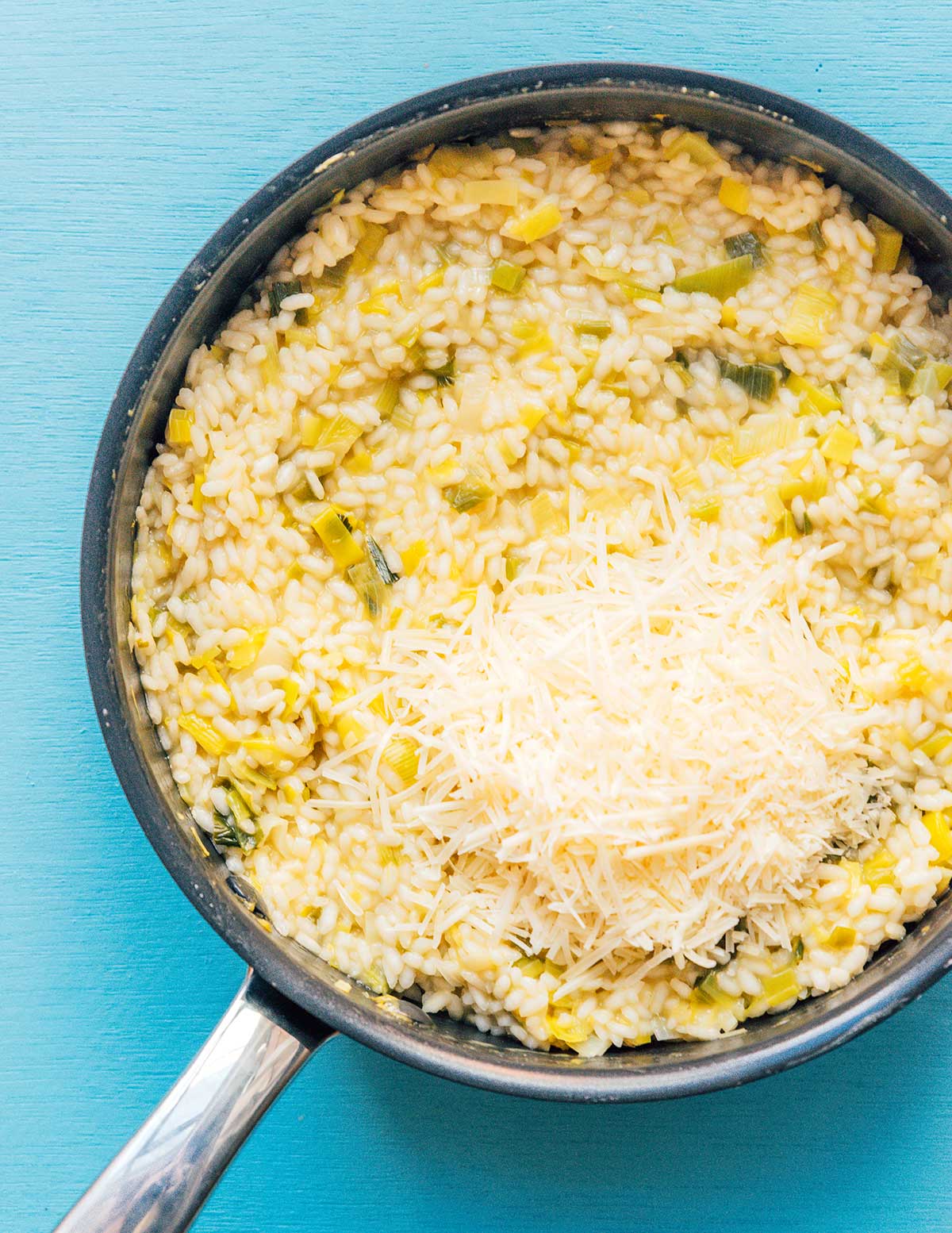 A skillet filled with leek risotto and shredded parmesan cheese