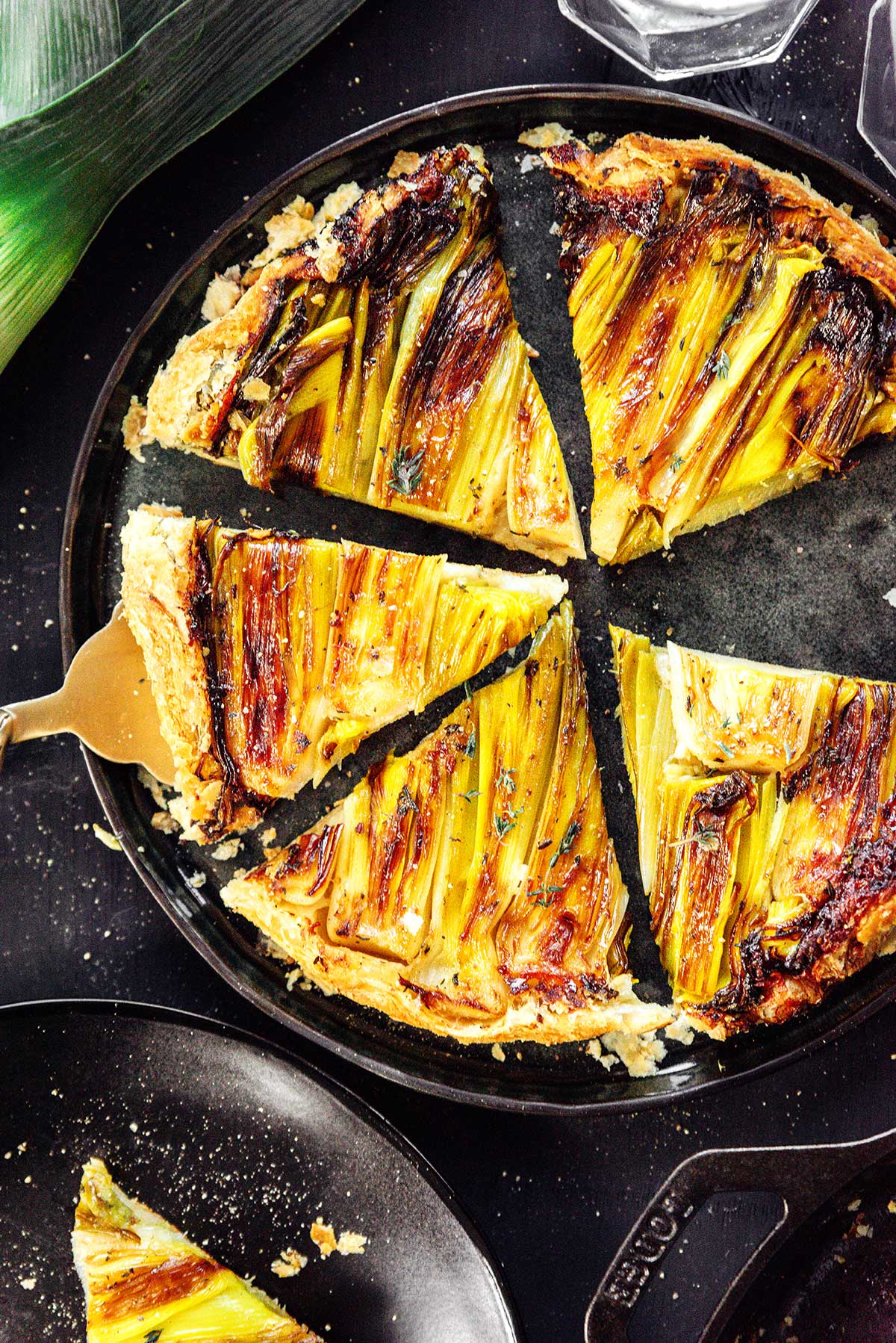 A gold spatula scooping a slice of leek tart from a skillet containing 5 pieces 