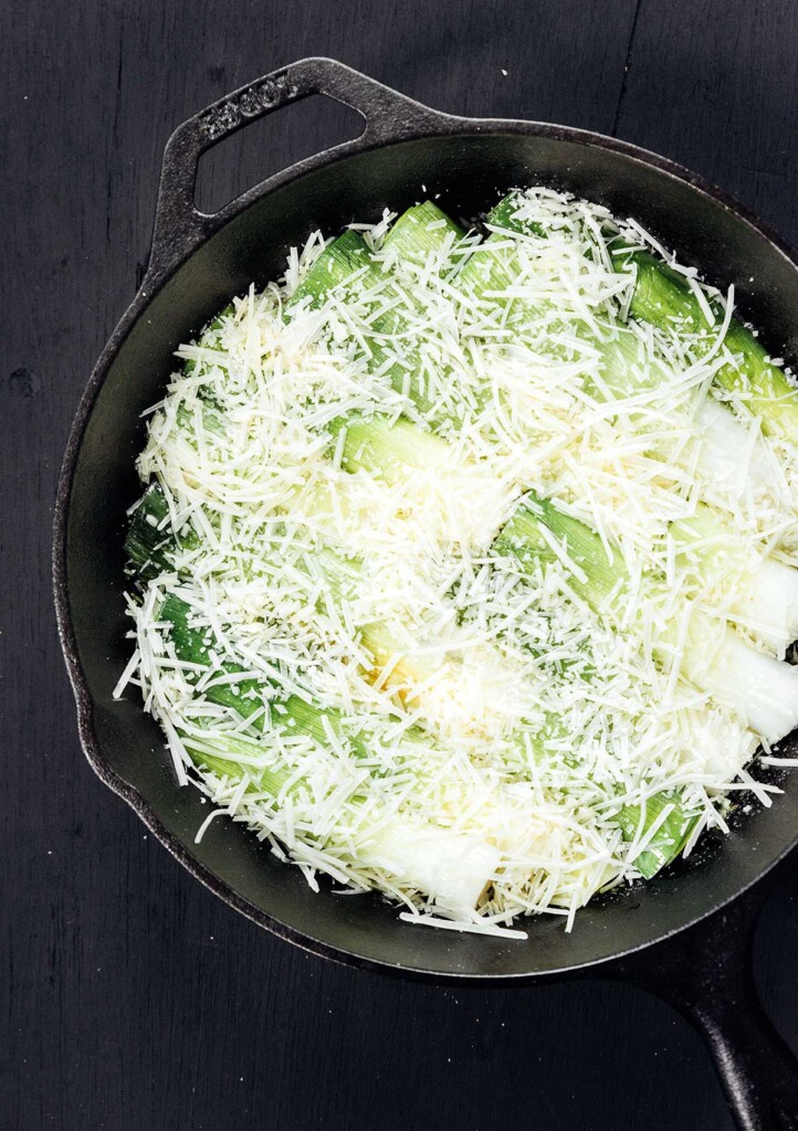 A skillet filled with leeks and topped with parmesan cheese