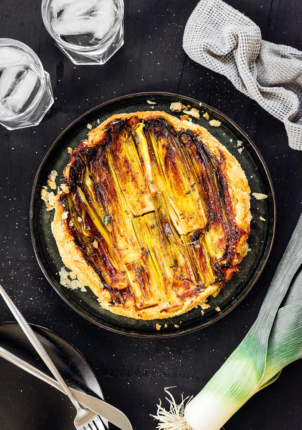 A bird's eye view of a large black plate filled with a freshly cooked, whole upside down leek tart