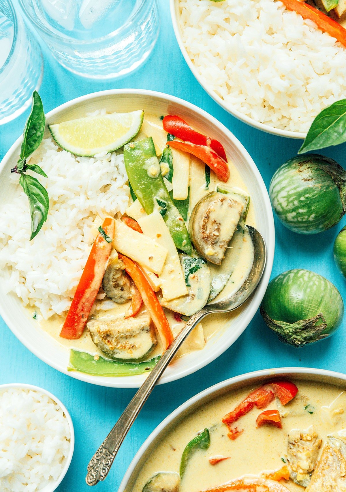A white bowl filled with Thai green curry on top of a bed of rice and garnished with basil and a lime wedge