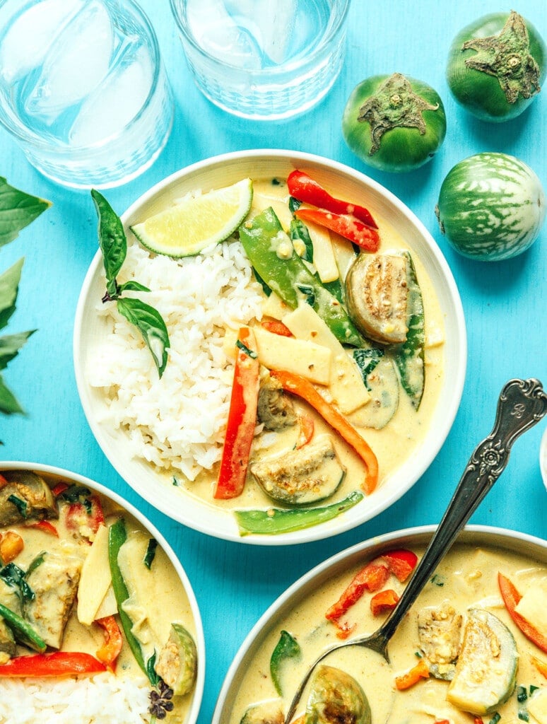 A white bowl filled with Thai green curry on top of a bed of rice and garnished with basil and a lime wedge