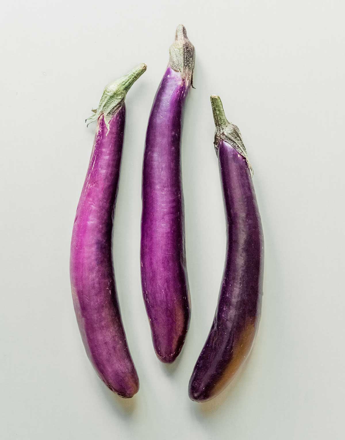 Three Chinese eggplants arranged in a row on a gray background