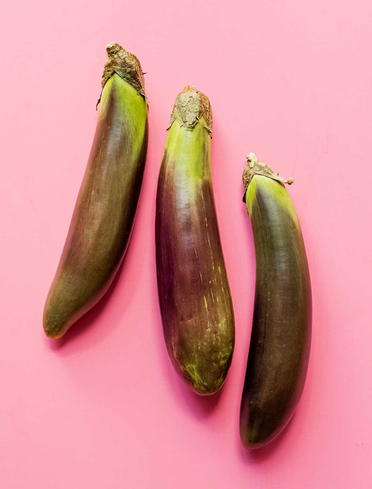 Three Filipino eggplants arranged in a row on a pink background