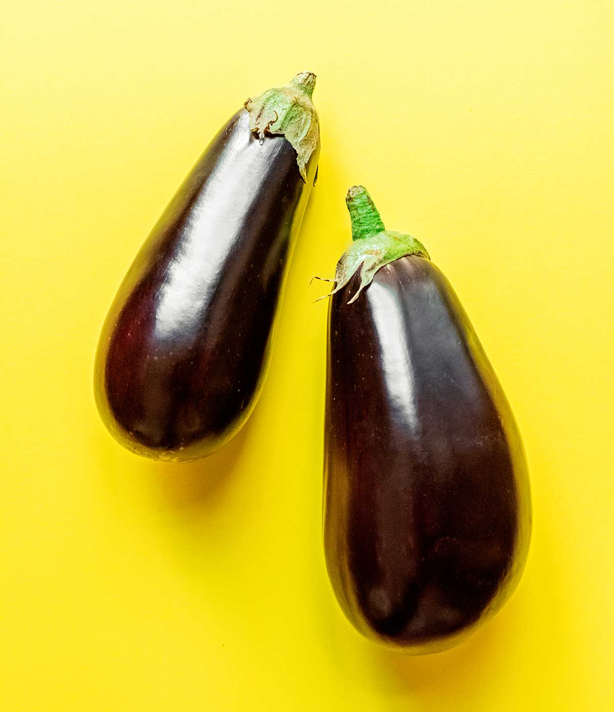 Two Italian eggplants arranged on a yellow background