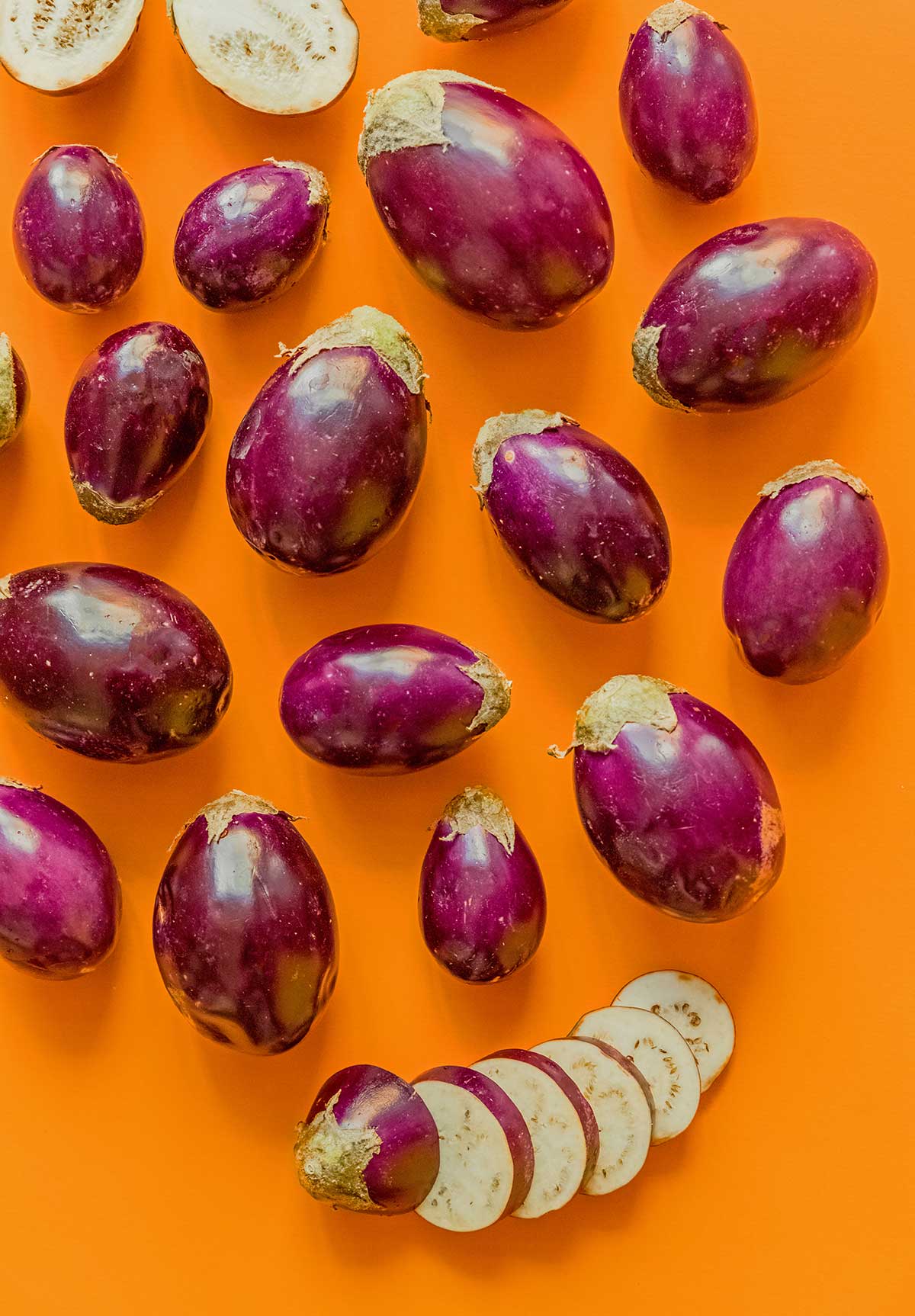 Nineteen Indian eggplants arranged on an orange background