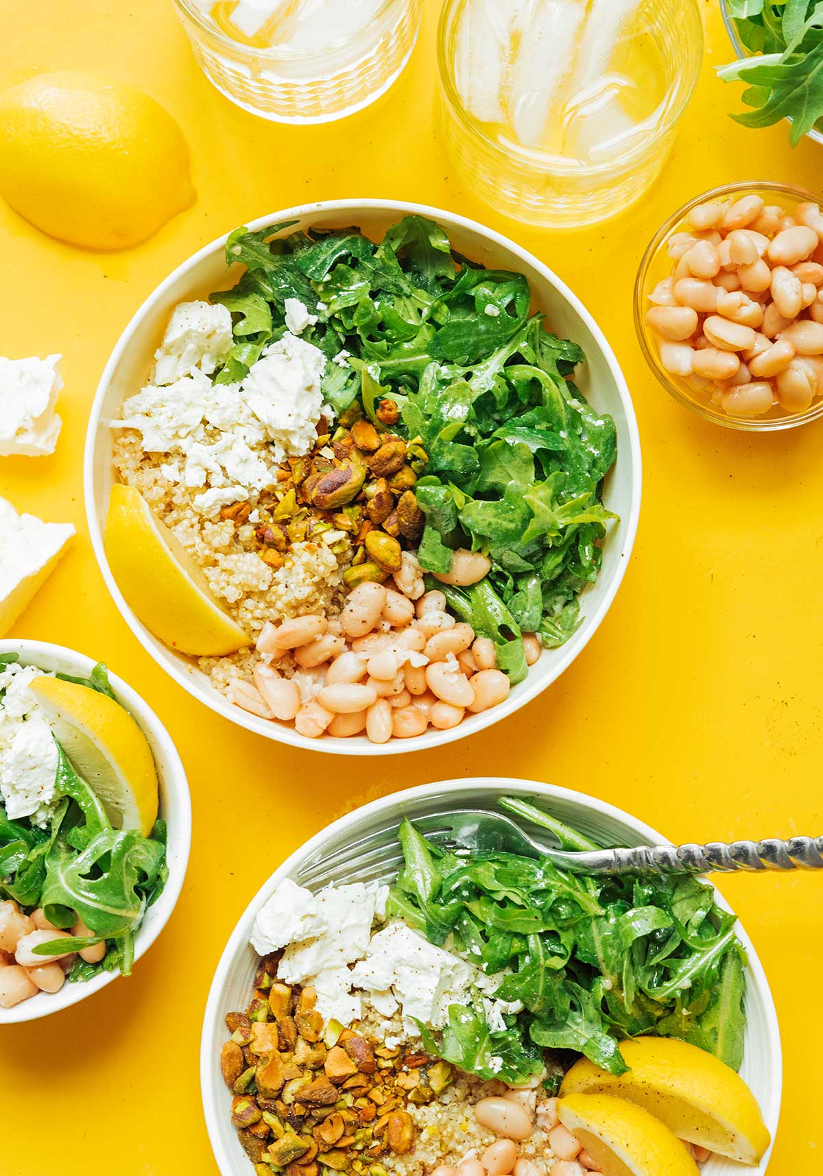 A arugula power bowl topped with pistachios, feta cheese, navy beans, and lemon dressing