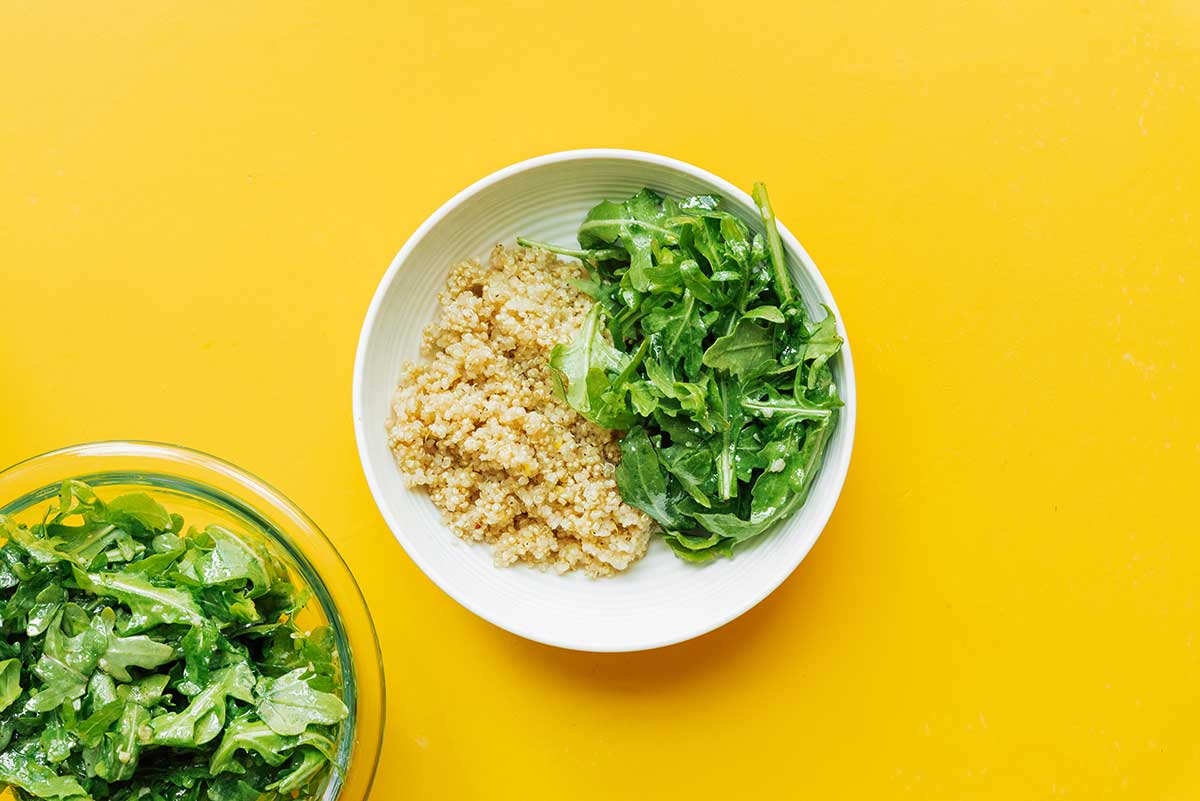 A white bowl filled with one serving of cooked quinoa and lemon dressed arugula