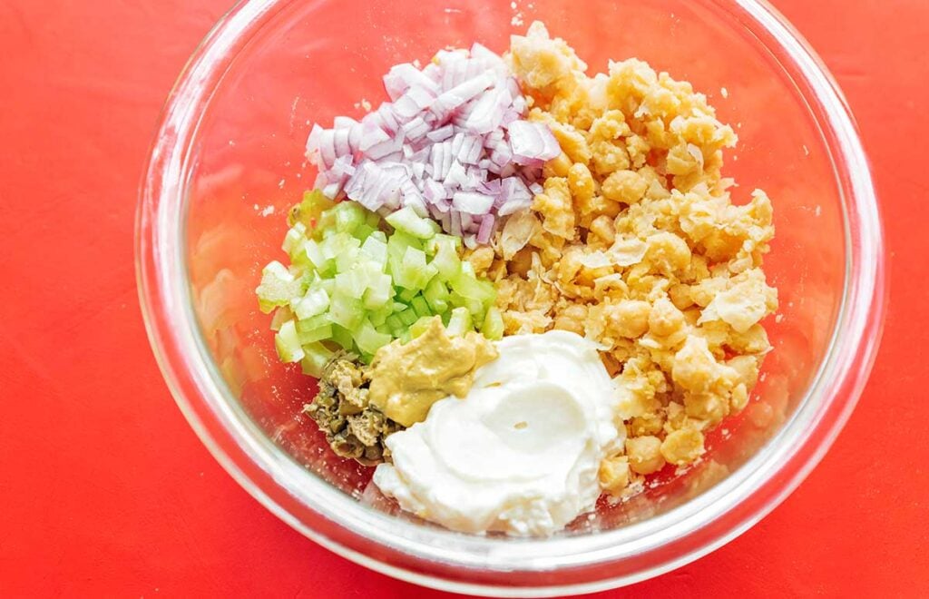 A clear glass bowl filled with fresh tuna salad ingredients for a chard wrap filling