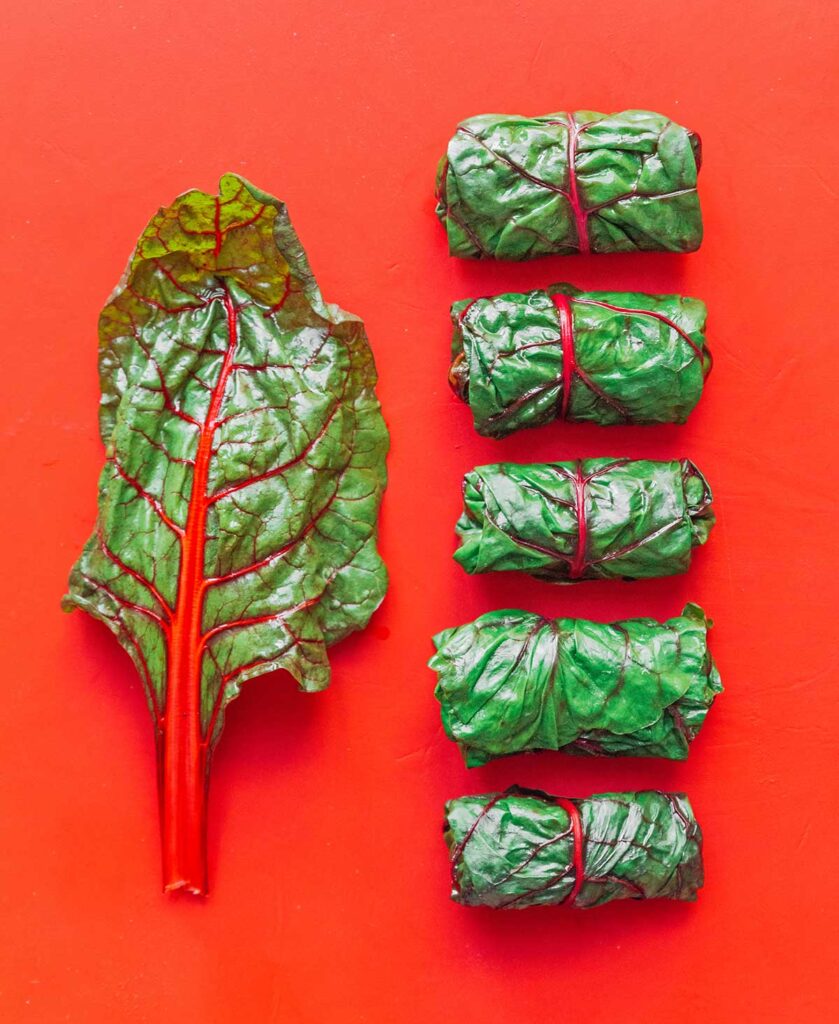 Five rolled chard wraps and one unrolled chard leaf arranged on a red background
