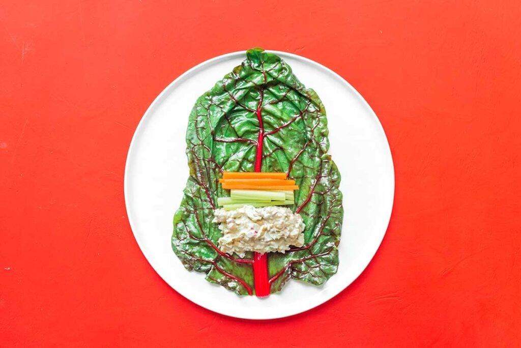 A chard leaf on a white plate filled with tune salad and veggies