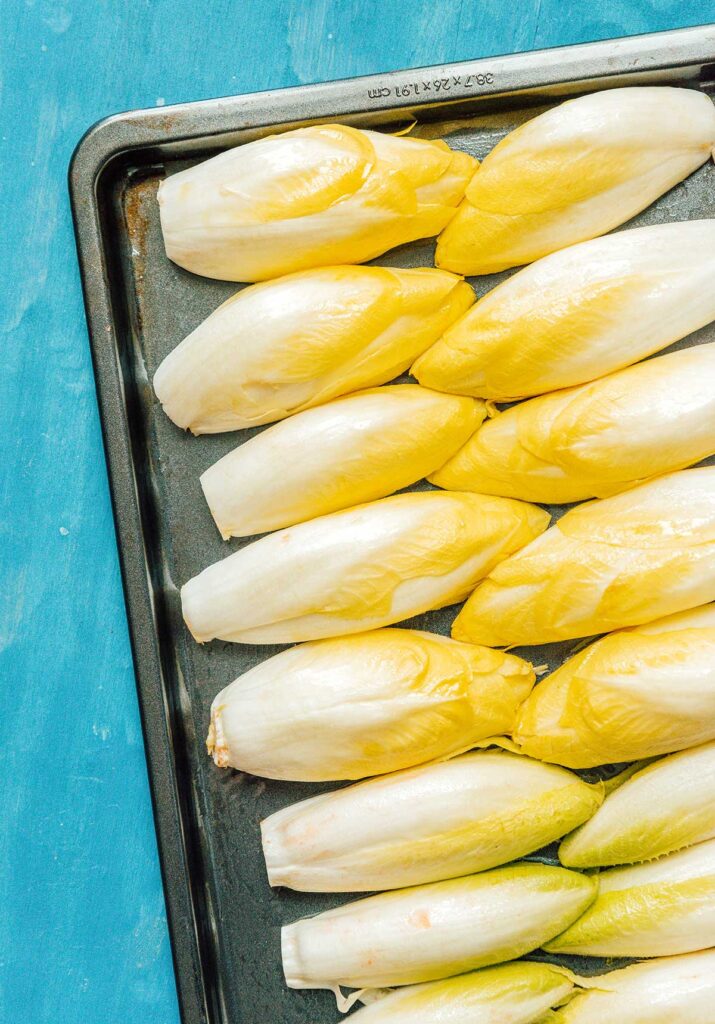 Uncooked Belgian endives halved and arranged cut side down on a baking sheet