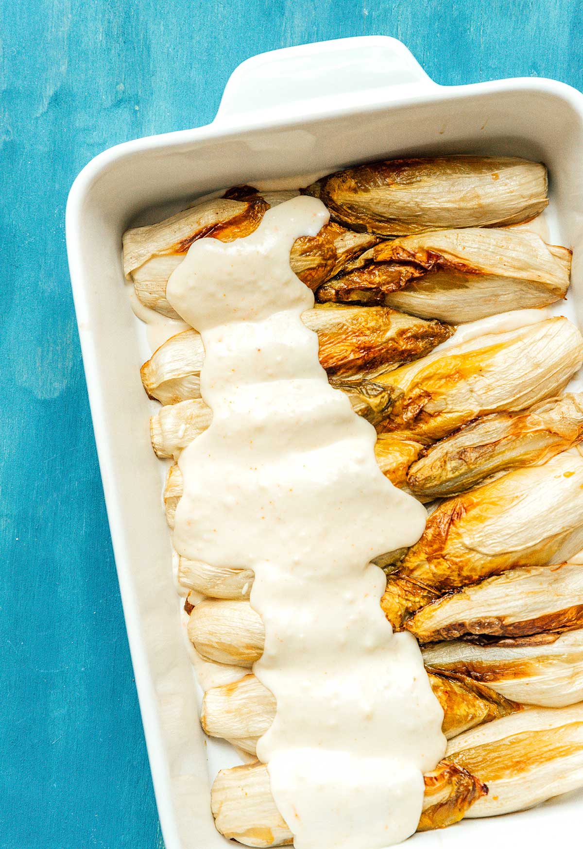 Layering Belgian endive gratin in a casserole dish with bechamel sauce