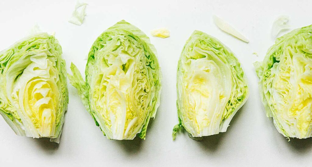 Four quarters of a head of iceberg lettuce lined up on a white background, inside facing up