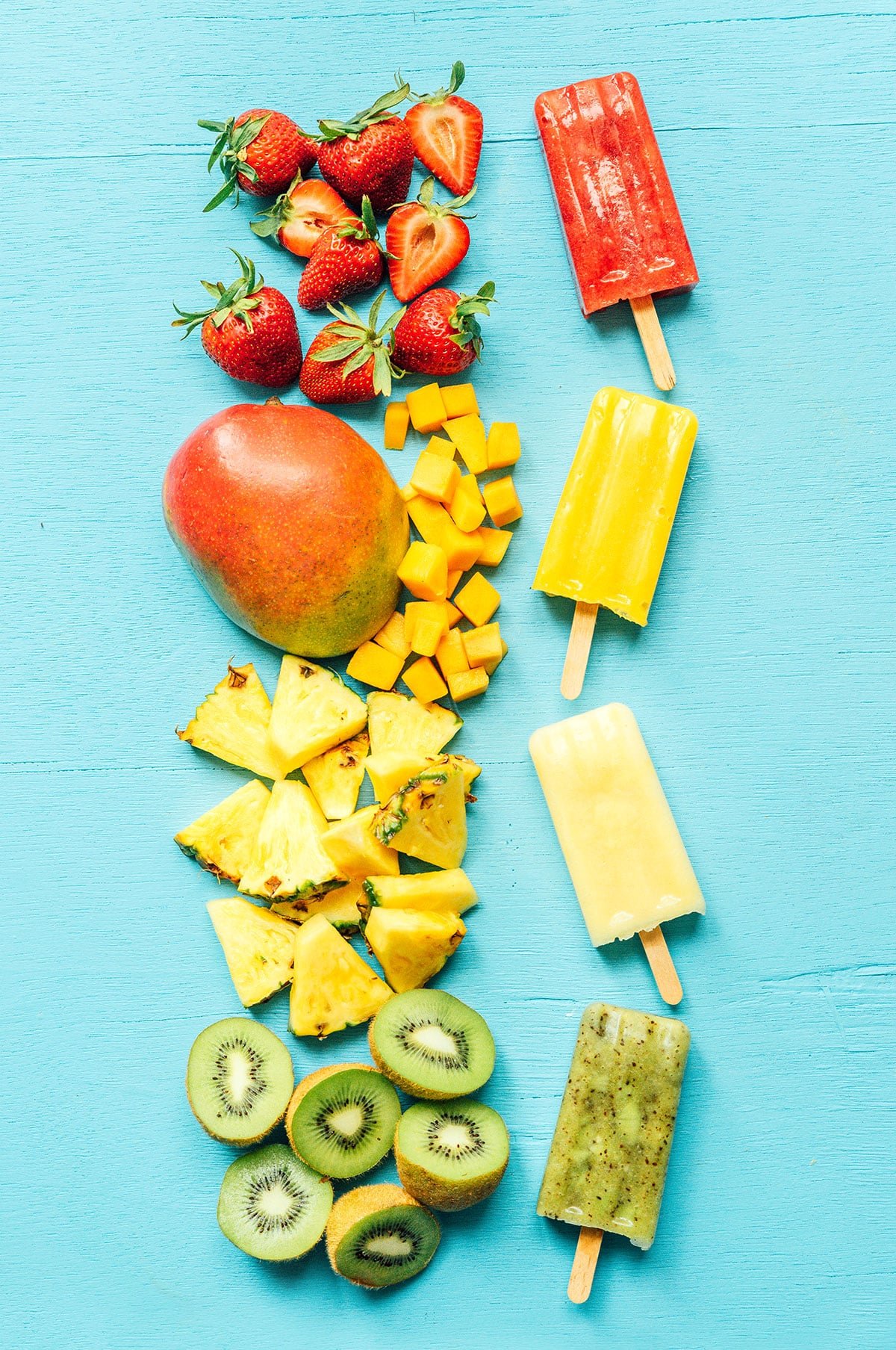 Multiple colors of fruit paletas on a blue background