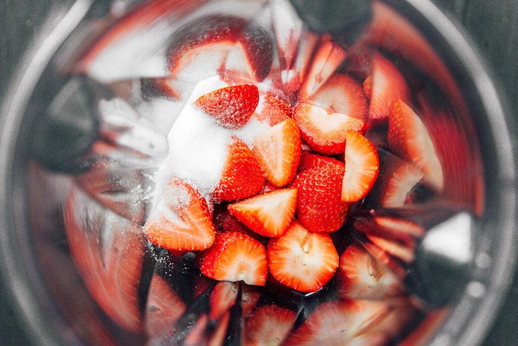 A blender filled with strawberries and sugar 