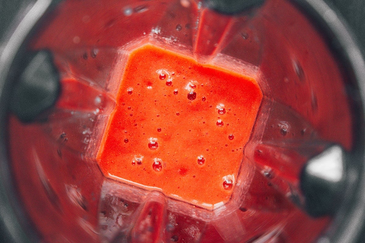 A blender filled with blended strawberry popsicle ingredients
