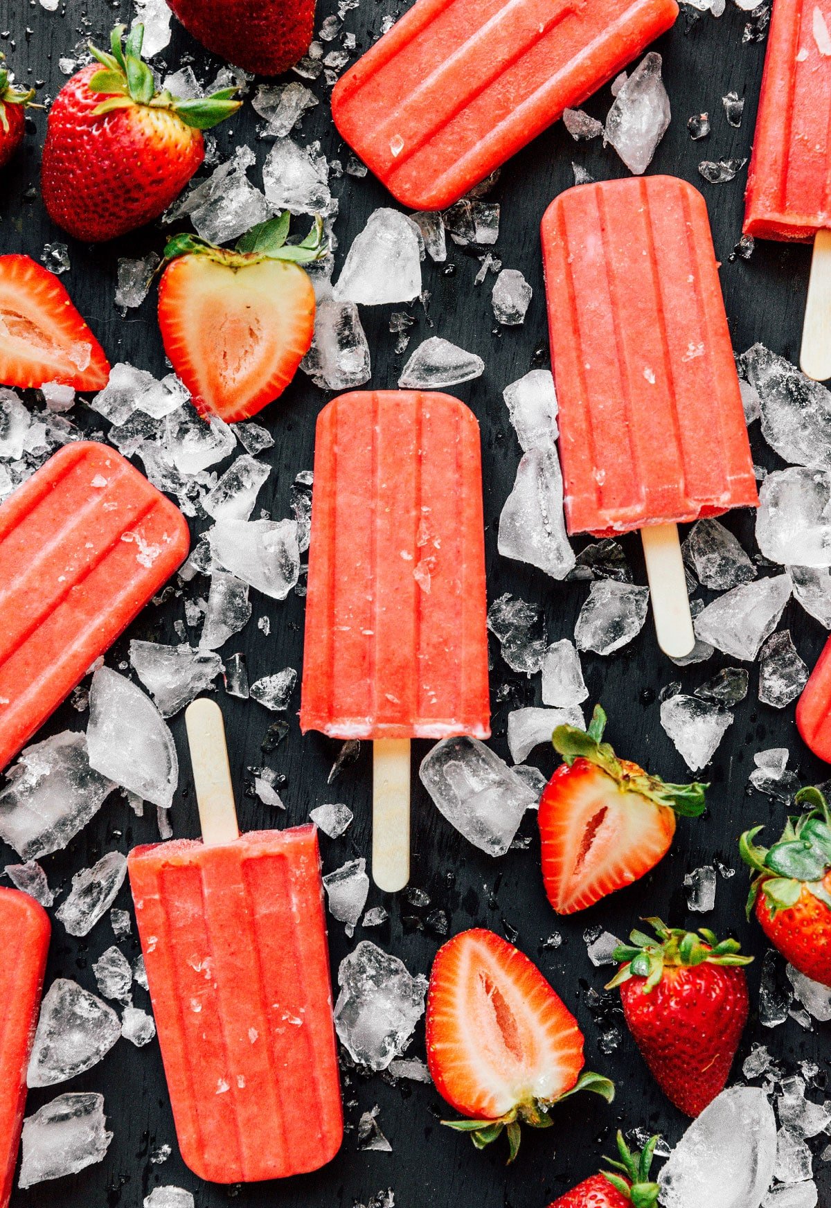 Real strawberry popsicles displayed on a black background and surrounded by ice and strawberries