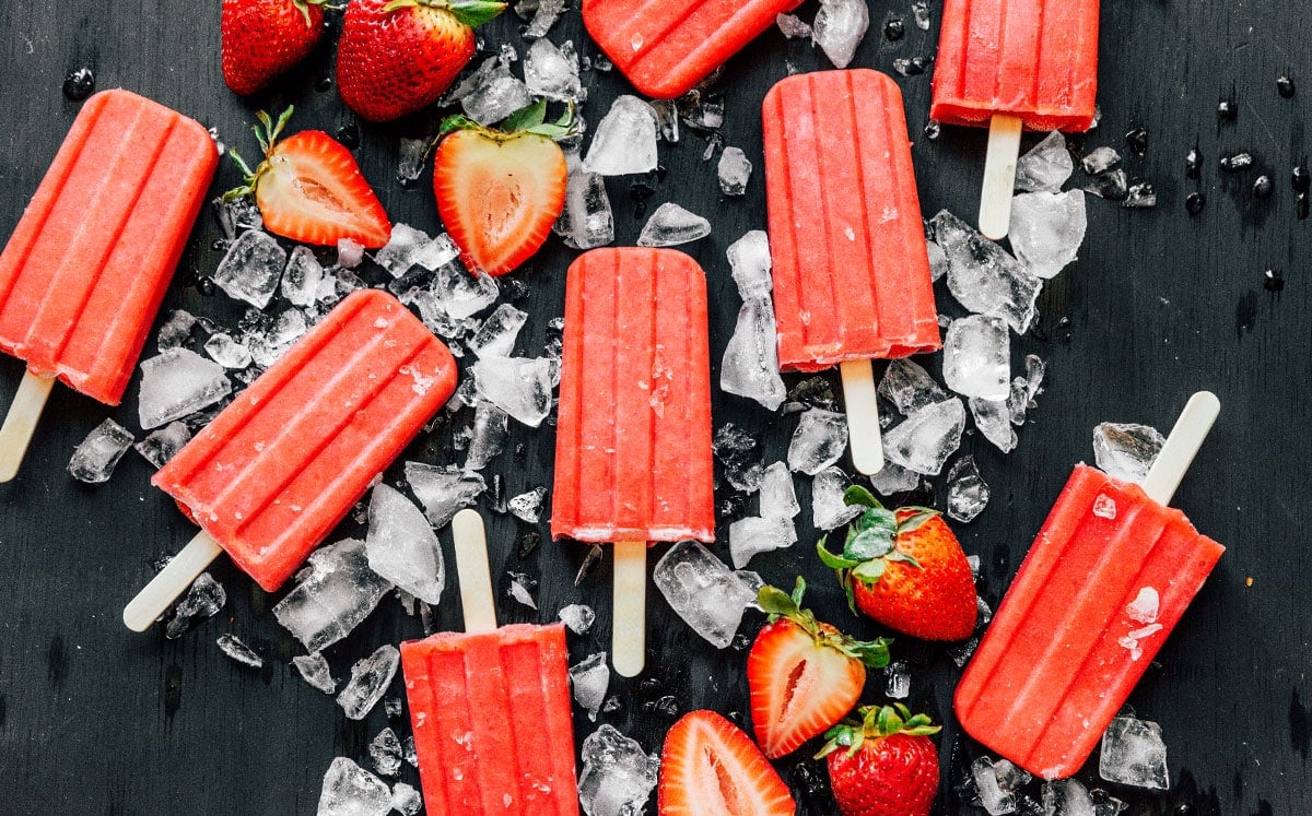 Sugar-free strawberry popsicles displayed on a black background and surrounded by ice and strawberries