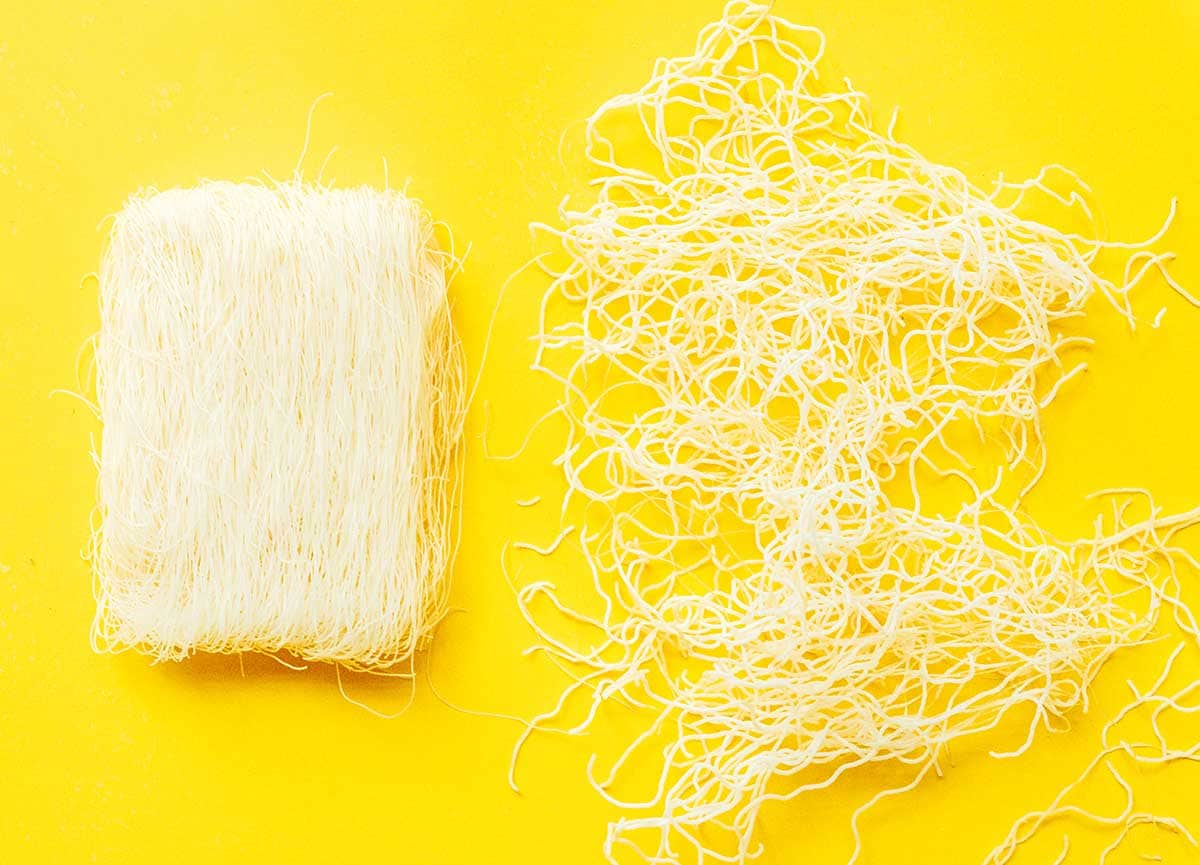 A square of rice noodles next to a handful of loose rice noodles on a yellow background